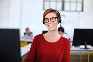 En leende kvinna framför en datorskärm som arbetar med ärendehanteringssystemet Artologik HelpDesk.