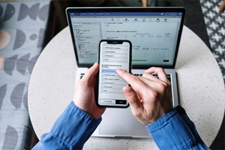 En mobiltelefon som visar Artologiks enkätverktyg Survey&Report. Mobiltelefonen hålls ovanför en dator som också innehåller en vy med enkätverktyget.